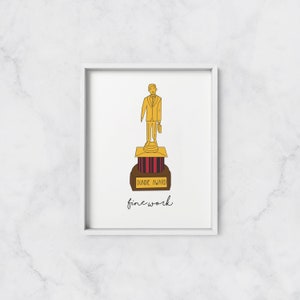 May include: A gold-colored award statue of a person in a suit holding a briefcase. The base of the statue says "Dundie Award" and the text "fine work" is written below the statue.