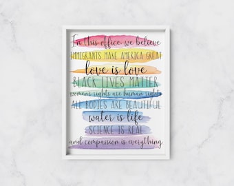 May include: A framed print with a rainbow watercolour background and text that reads "In this office we believe Immigrants make America great love is love Black Lives Matter women's rights are human rights All bodies are beautiful water is life Science is real and compassion is everything."