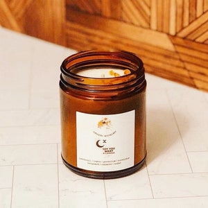 Peut inclure: Un bocal en verre brun contenant une bougie avec une étiquette blanche sur laquelle est inscrit "SOY YOU WANT A CANDLE" et qui liste les parfums : patchouli, citron, géranium, eucalyptus, bergamote, cannelle, cèdre.