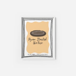 Puede incluir: Una impresión enmarcada en blanco con una forma ovalada marrón y el texto "Ryan Started the Fire" en fuente cursiva negra. El texto "Dunder Mifflin: A Retrospective Series" también está incluido en fuente negra.