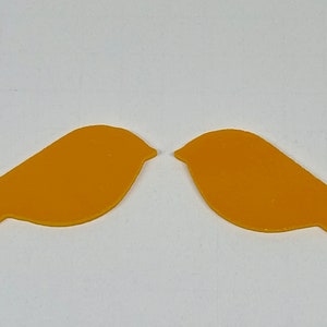 May include: Two yellow bird cutouts, facing each other, with a simple design. The birds are made of a thin, flat material, possibly paper or plastic.