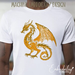 May include: A white t-shirt with a gold embroidered dragon design. The dragon is detailed with intricate patterns and has its wings spread out.