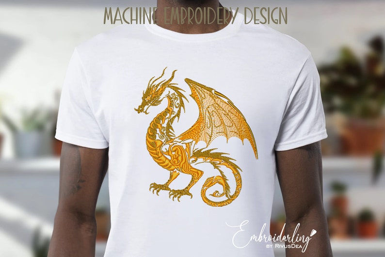 May include: A white t-shirt with a gold embroidered dragon design. The dragon is detailed with intricate patterns and has its wings spread out.
