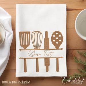 Op de afbeelding: Een witte keukendoek met een bruin geborduurd ontwerp van keukengerei, waaronder een spatel, een garde, een deegroller en een schuimspaan. De tekst "Your Text" is geborduurd boven het keukengerei.