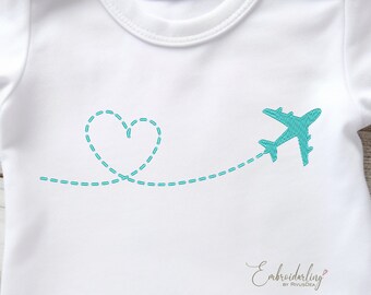 May include: A white t-shirt with a turquoise blue embroidered design of a plane flying in a heart-shaped path.