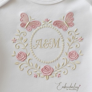 Può includere: Body da bambino bianco con un ricamo floreale rosa. Il design include due farfalle, rose e le iniziali "A&M" all'interno di un cerchio. Il testo "Embroiderling" è in basso.