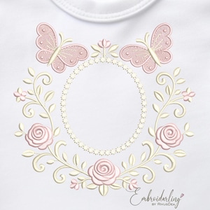 May include: Embroidered design featuring two pink butterflies, roses, and floral vines surrounding an oval frame. The design is in shades of pink and cream on a white background. The text "Embroiderling" is at the bottom.