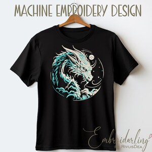 May include: Black t-shirt with a white and blue embroidered design of a dragon in a circle with a moon and stars. "MACHINE EMBROIDERY DESIGN" is written at the top of the image.