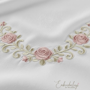 以下が含まれることがあります： 白い生地に刺繍された花の模様のクローズアップ。刺繍はピンクのバラ、緑の葉、繊細な渦巻き模様が特徴です。デザインは曲線的なパターンで配置されており、エレガントさを加えています。