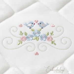 May include: Embroidered design featuring two light blue birds with red beaks, perched above a floral arrangement of blue flowers, pink roses, and green leaves. Pink hearts and pearl-like swirls complete the design on a white quilted background.