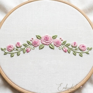 Può includere: Un telaio da ricamo circolare in legno contenente tessuto bianco con un motivo floreale cucito a mano. Il ricamo presenta una rosa rosa centrale circondata da boccioli di rosa più piccoli e foglie verdi disposti in un arco simmetrico.