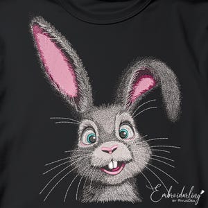 May include: Embroidered design of a gray rabbit with pink ears and a white smile on a black t-shirt. The text "Embroidarling by RivusDea" is in the bottom right corner.