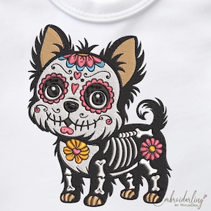 May include: Embroidered design of a black and tan dog with a sugar skull face, skeleton body, and floral accents. The dog has a pink and blue floral crown and a yellow flower collar. The design is on a white background.