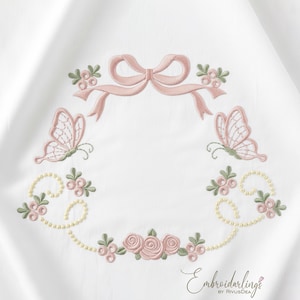May include: White fabric with an embroidered design. It features a pink bow, butterflies, roses, and floral accents. The design is arranged in a circular pattern, with the text "Embroiderlings" at the bottom.