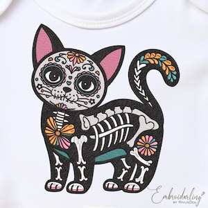 May include: A black cat design with a sugar skull face and skeleton body, adorned with colorful floral accents. The design is on a white onesie, perfect for a baby or toddler. The cat's ears are pink, and the tail has a decorative pattern.