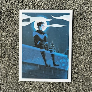 Puede incluir: Un personaje de superhéroe azul y negro se sienta en una azotea por la noche. El personaje mira hacia la izquierda, con una ciudad en el fondo. La luna es visible en el cielo.