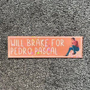 May include: A pink and white sticker with the text "WILL BRAKE FOR PEDRO PASCAL" and a cartoon image of a man sitting on a step.