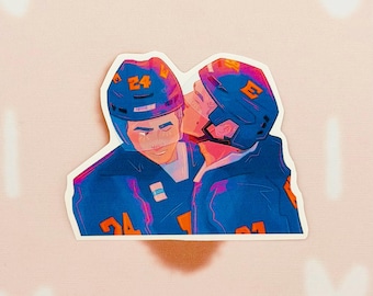 Könnte beinhalten: Ein Aufkleber mit zwei Eishockeyspielern in blauen Uniformen und Helmen, von denen einer den anderen auf die Wange küsst. Der Aufkleber hat einen weißen Rand und ist vor einem rosa Hintergrund platziert.