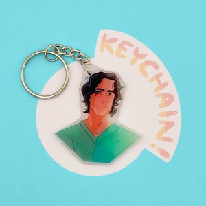 May include: A keychain featuring an illustration of a person with dark hair and a green shirt. The keychain has a gold-colored metal ring and chain. The word "KEYCHAIN!" is printed in a semi-circle above the illustration.