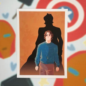 May include: Illustration of a person in a blue sweater and brown pants, with a dark shadow figure behind them. The background is orange. The artwork is on a white rectangular print.