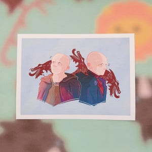 以下が含まれることがあります： 丸刈りの2人の人物のイラスト。それぞれ背後に赤いドラゴンがいます。一人は暗いマントを、もう一人は赤いスカーフ付きの青いジャケットを着ています。背景は水色です。
