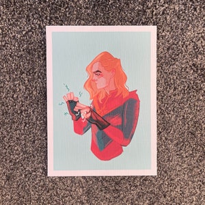 May include: A digital illustration of a woman with long blonde hair wearing a red and blue superhero costume. She is holding her hands up, and there are sparks of energy coming from her fingertips.