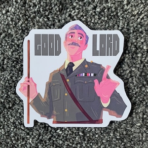 May include: A sticker featuring a cartoon man with gray hair and a mustache, wearing a gray military uniform with gold buttons and a red sash. The man is holding a stick in his left hand and pointing with his right hand. The text "GOOD LORD" is printed in gray letters on the sticker.