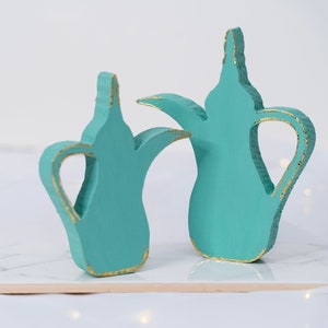 May include: Two teal blue ceramic teapots with gold accents. The teapots are in the shape of traditional Middle Eastern coffee pots.