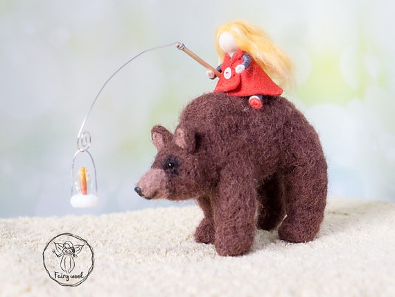 Felt sculpture of wild brown bear and tiny girl in red cloak. The figurine of huntress with lamp.