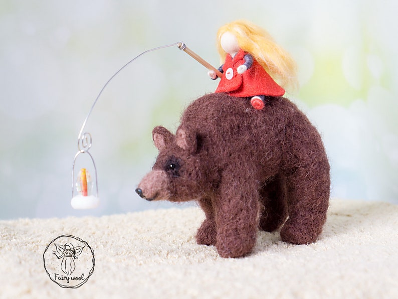 May include: A felt doll with blonde hair wearing a red coat rides a brown felt bear. The bear is walking towards a small lantern with a lit candle.