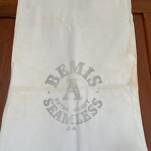 Puede incluir: Bolsa de lona blanca con un logotipo circular plateado que dice "Bemis A Seamless Extra Heavy D4".