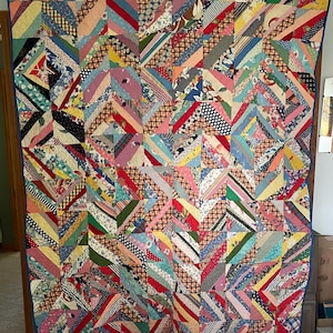 May include: A colorful handmade quilt with a patchwork design. The quilt features a variety of fabric patterns and colors, including stripes, florals, and polka dots. The quilt is displayed on a wall, showcasing its intricate craftsmanship and vibrant aesthetic.