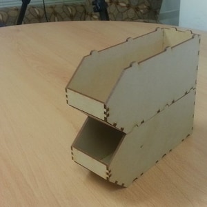 May include: A two-tiered wooden organizer with a light brown finish. The organizer has a rectangular shape and is made of plywood.