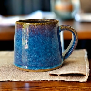 May include: A blue and brown ceramic mug with a glazed finish. The mug has a rounded body and a handle.