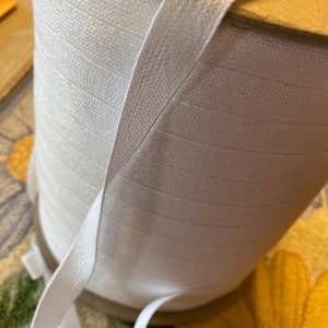 May include: A spool of white elastic trim with a white elastic band wrapped around it.