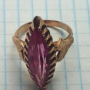 Puede incluir: Un anillo de oro con una gran piedra preciosa rosa facetada de forma marquesa engastada en un engaste decorativo y ornamentado.