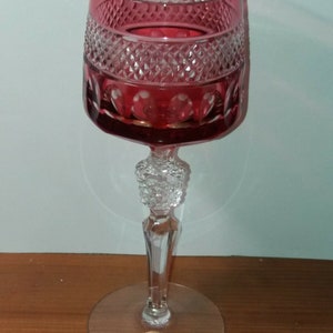 Könnte beinhalten: Ein klares Weinglas aus Glas mit rotem Stiel und Fuß. Das Glas hat ein geschliffenes Kristallmuster und ein rot-gold-weißes Etikett mit der Aufschrift "24% Lead Crystal Bohemia - Germany".