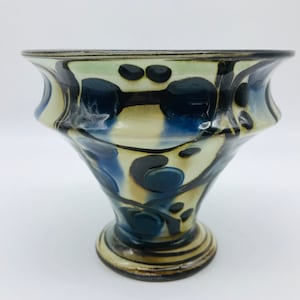 May include: A ceramic vase with a flared top and a wide base. The vase is decorated with a swirling pattern of black, blue, and white.