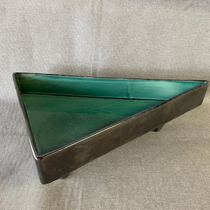 Puede incluir: Una bandeja triangular de cerámica con un esmalte verde oscuro y una base negra. La bandeja tiene tres patas y es perfecta para exhibir objetos pequeños.