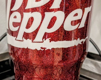 May include: A red glitter tumbler with the Dr Pepper logo in white. The tumbler has a shiny, textured surface and a classic design. The text is in a bold, easy-to-read font.