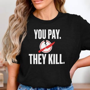 May include: Black t-shirt with the text "YOU PAY. THEY KILL." in white. A graphic of a cracked egg with a red knife through it is centered above the text. The shirt is made of a soft material.