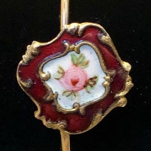 May include: A gold-tone bangle bracelet with a red enamel and white porcelain charm featuring a pink rose with green leaves.