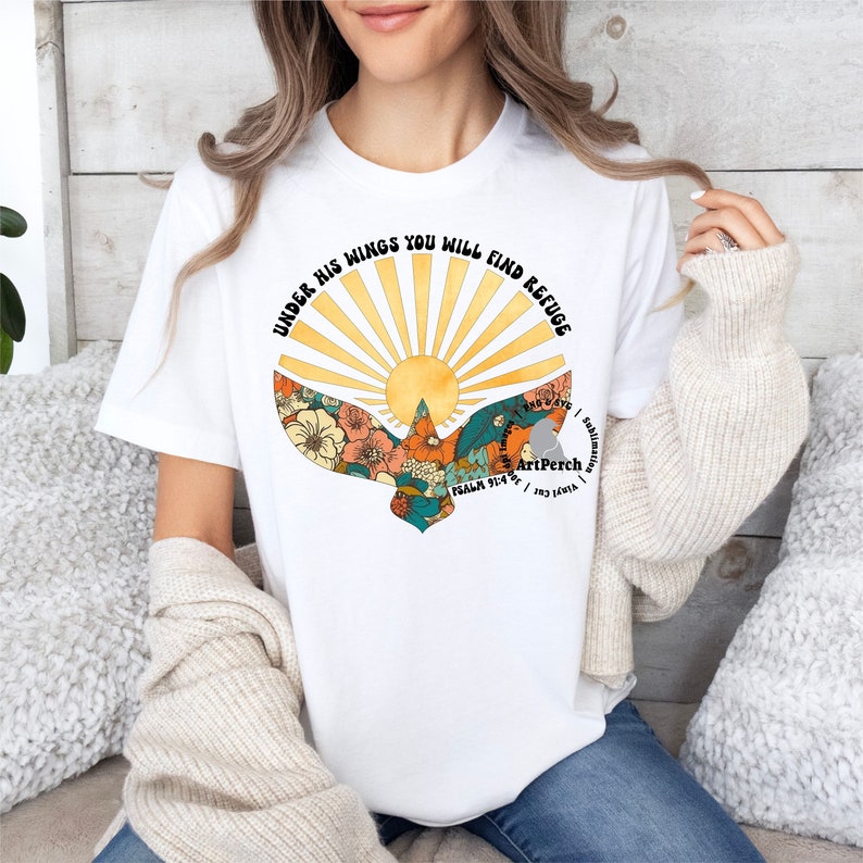 May include: White t-shirt with a graphic of a sun rising behind a bird with floral patterns. The text "Under His Wings You Will Find Refuge" is written around the sun and bird. The text "Psalm 91:4" and "ArtPerch" are also included in the graphic.