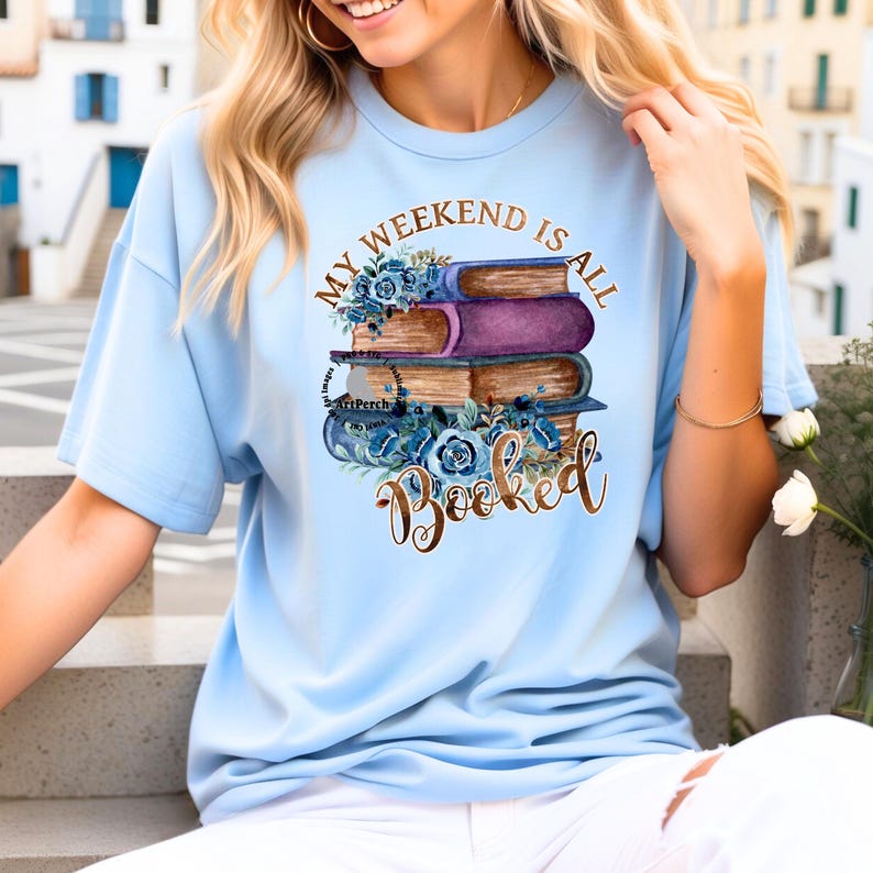 May include: Light blue t-shirt with a graphic of a stack of books with blue flowers and the text "My Weekend Is All Booked" in gold lettering.