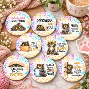 May include: A set of seven round ceramic coasters featuring illustrations of a fluffy cat with large yellow eyes. Each coaster displays unique text including Butterfly Kisses & Kitty Hisses, Peekaboo I see you, Yarn Zombie, If I fits I sits, I'm not messy I'm just Fluffy & fabulous, I'm Not Hiding I'm Just PLOTTING, My blood type is COFFEE & CHAOS, and HANG IN THERE.