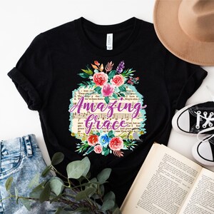 May include: Black t-shirt with a floral design and the text "Amazing Grace" printed on it. The text is in purple and the floral design is in shades of pink, blue, and green.