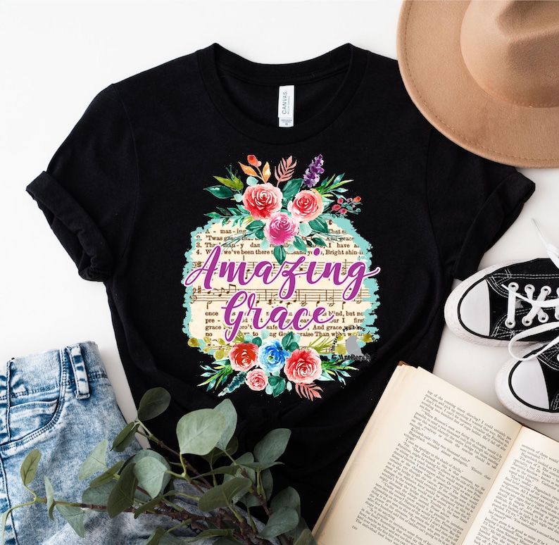 May include: Black t-shirt with a floral design and the text "Amazing Grace" printed on it. The text is in purple and the floral design is in shades of pink, blue, and green.