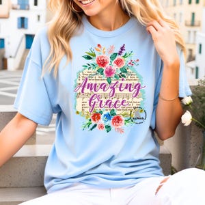 May include: Light blue t-shirt with a floral design and the text "Amazing Grace" printed on it. The text is set against a vintage sheet music background.