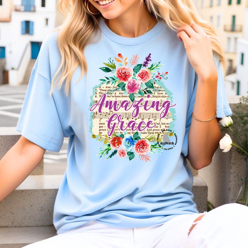 May include: Light blue t-shirt with a floral design and the text "Amazing Grace" printed on it. The text is set against a vintage sheet music background.