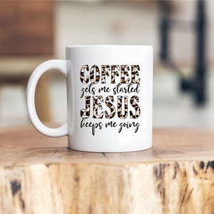 Pode incluir: Caneca de caf&eacute; de cer&acirc;mica branca com um design de estampa de leopardo preto e marrom. O texto "COFFEE gets me started JESUS keeps me going" est&aacute; impresso na caneca.